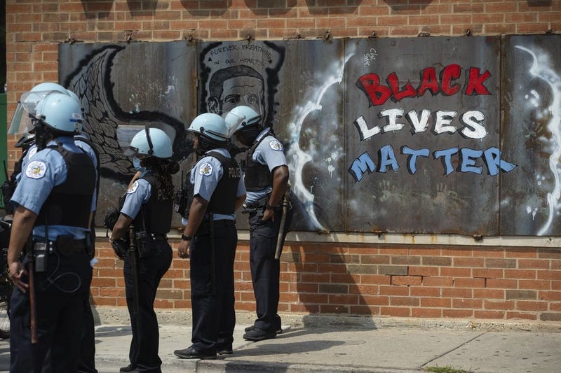 FILE - In this Aug. 15, 2020, file photo, police officers stand beside a mural for George Floyd in the Chicago neighborhood of Bronzeville during an anti-police brutality protest. In the last decade, high-profile police killings — including Floyd — have shaken the nation and led to widespread protests and calls for reform, including hiring more nonwhite and female officers.