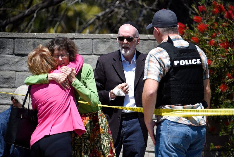 Two people hug as another talks to a San Diego County Sheriff's deputy outside of the Chabad of Poway synagogue, Saturday, April 27, 2019, in Poway, Calif. A man opened fire inside the synagogue near San Diego as worshippers celebrated the last day of a m