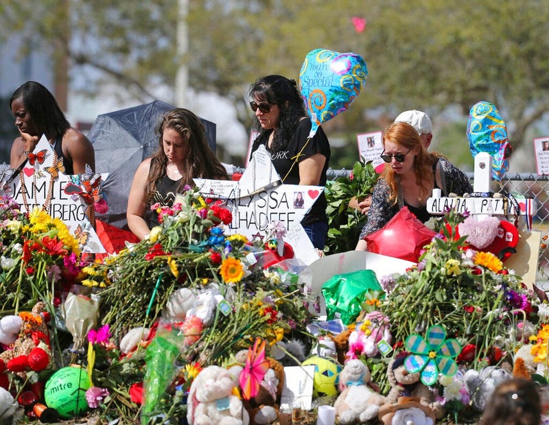 mourners bring flowers as they pay tribute at a memorial for the victims of the shooting at Marjory Stoneman Douglas High School, in Parkland, Fla.