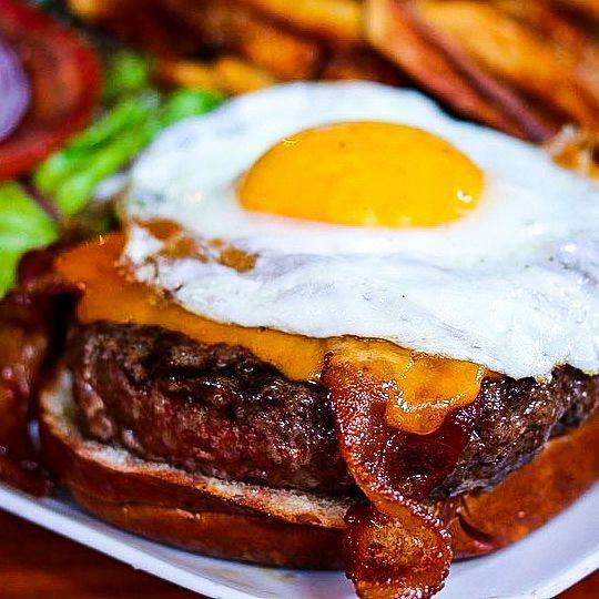 Kuma's Corner's namesake burger, "The Famous Kuma" featuring bacon, sharp cheddar, lettuce, tomato, red onion, and a fried egg.
