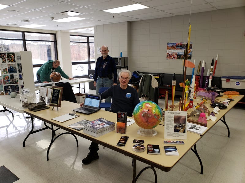 Jim Plaxco (sitting, center) poses for a photo behind a display at a school STEM festival.
