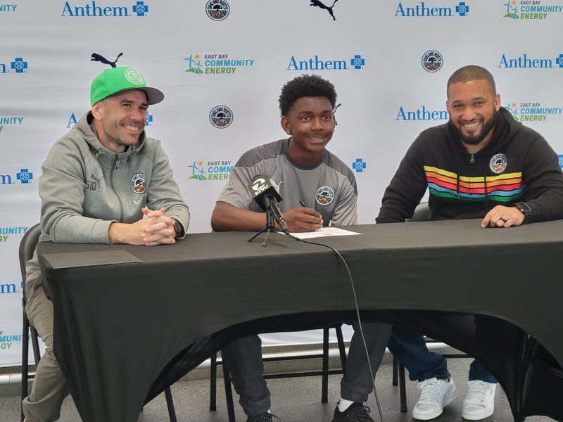 Nate Evans (middle) signs his contract with the Oakland Roots.