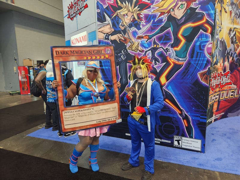 Yu-Gi-Oh! fans at New York Comic Con. One is dressed as the card Dark Magician Girl and the other is dressed as the character Yugi from the anime based on the card game.