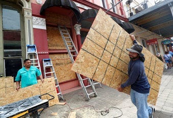 Cesar Reyes carries a sheet of plywood to cut to size as he and Robert Aparicio, left, and Manuel Sepulveda install window coverings at Strand Brass and Christmas on the Strand in Galveston. ( Jennifer Reynolds/The Galveston County Daily News via AP)