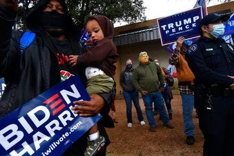 Demetrius Earthly balances his one-year-old son Brodrick and a Biden-Harris campaign sign, Wednesday, Oct. 28, 2020. Behind him, Toby Lindley wears a Donald Trump mask. (Ronald W. Erdrich/The Abilene Reporter-News via AP)