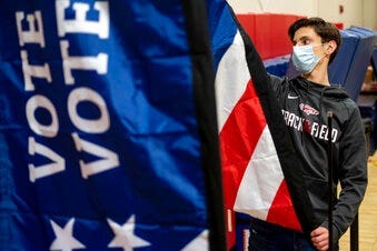 Thomas Hedrich sets up voting flags at a polling location in Gwinnett County, Ga., outside of Atlanta on Monday, Jan. 4, 2021, in advance of the Senate runoff election. (AP Photo/Ben Gray)