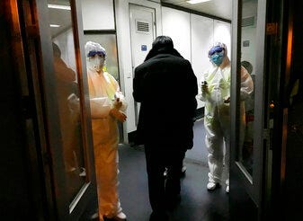 FILE - In this Wednesday, Jan. 22, 2020 file photo, Health Officials in hazmat suits wait at the gate to check body temperatures of passengers arriving from the city of Wuhan, at the airport in Beijing, China. (AP Photo Emily Wang, File)