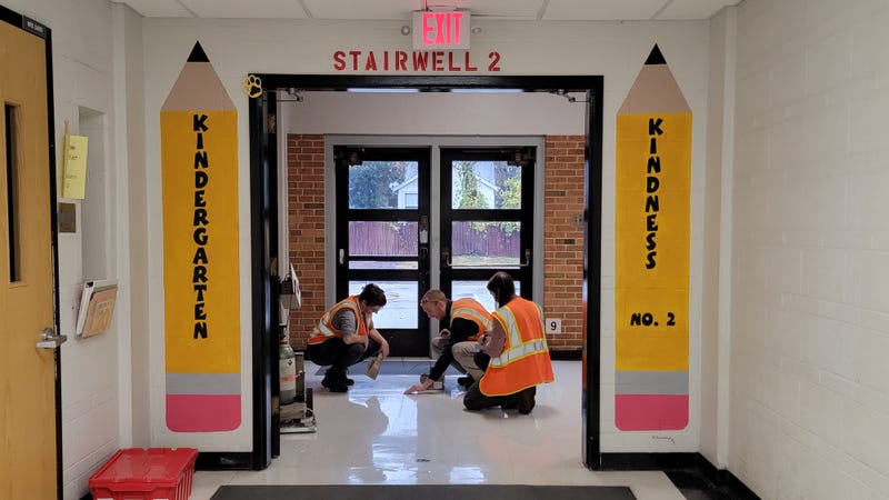 Contractors scan floors inside Jana Elementary School with radiation detection equipment. There are two big pencils painted on the walls that say kindergarten and kindness