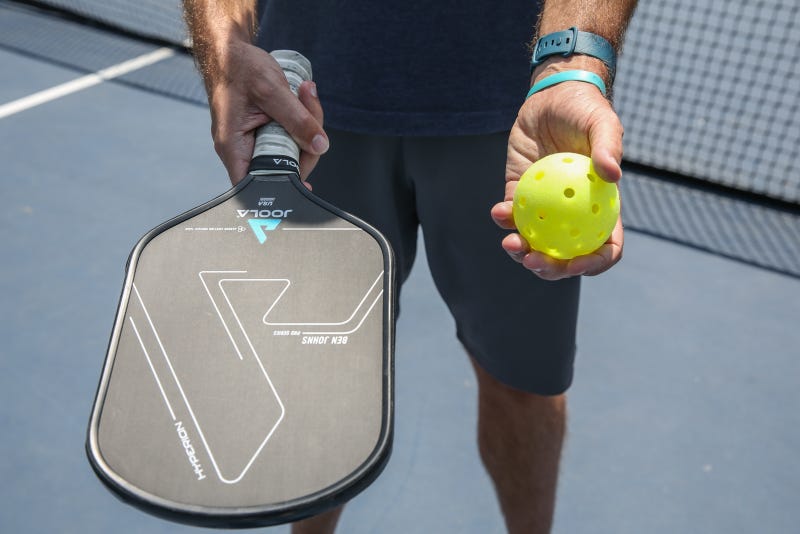 Closeup of a man holding a pickleball in one hand and a racket in the other.