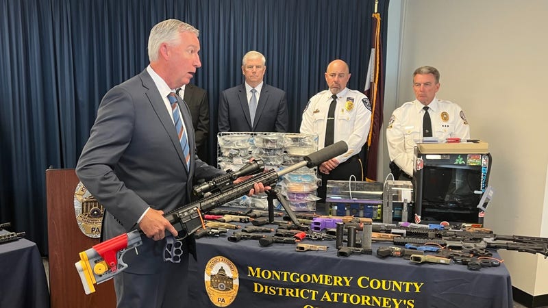 Montgomery County District Attorney holds a firearm with a 3D-printed stock and suppressor.