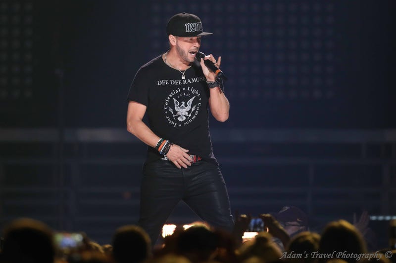 Man on stage with microphone wearing black tshirt and black hate. 