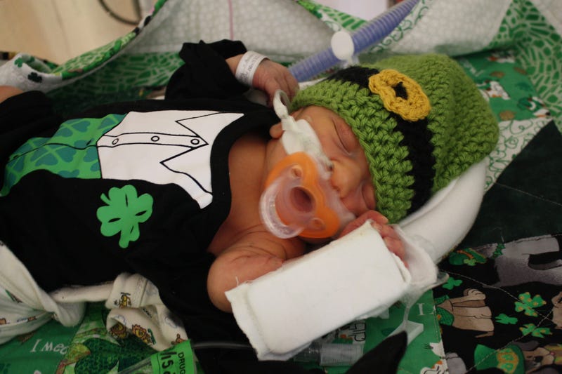 Newborn dressed for St. Patrick's Day lying on themed quilt