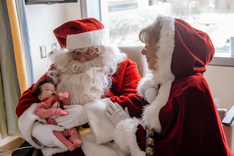 Baby in striped onesie with Santa and Mrs. Claus