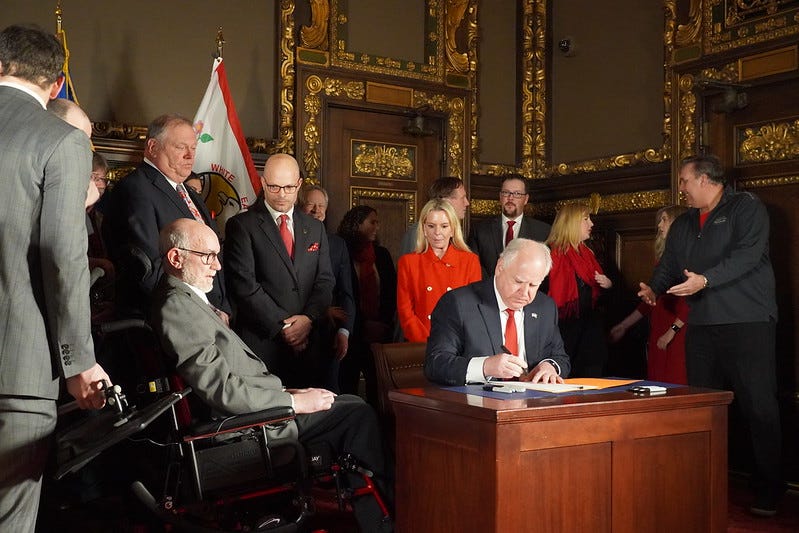 Sen Tomassoni who has ALS, watches from his wheelchair as Gov. Walz sign bill into law