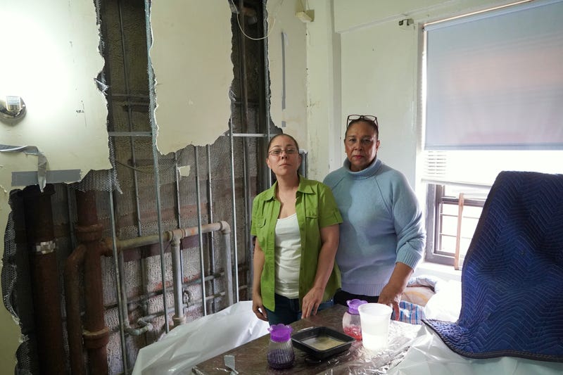 Two NYCHA residents stand in front of a destroyed wall in their apartment during a visit from Councilmember Carlina Rivera.