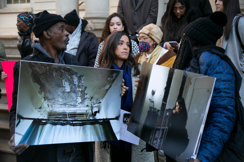 Rivera stands with NYCHA residents holding printed photographs of dilapidated apartments.
