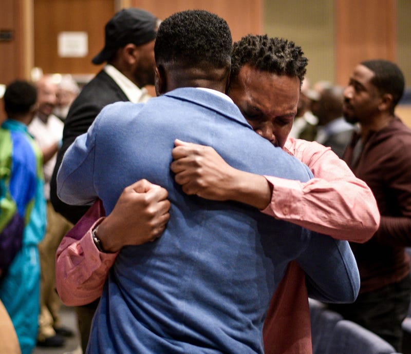 Lawrence E. Adjah (blue jacket) embraces a man at the Just Heal Bro conference for Black men's mental health. It is being held at the Microsoft School of the Future in West Philadelphia.
