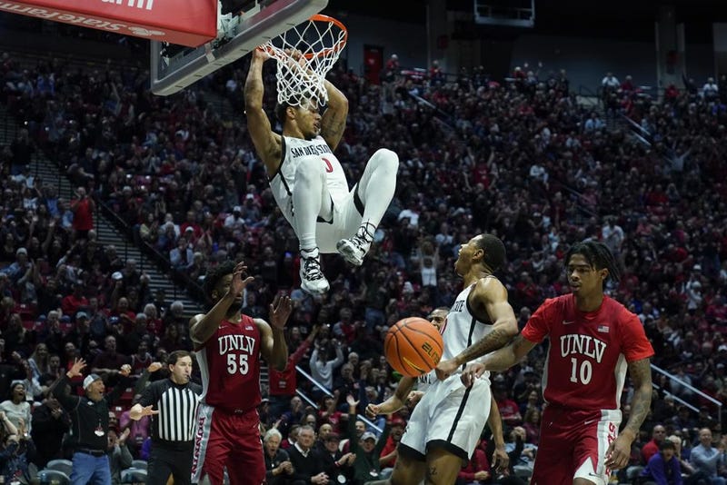 San Diego State guard Matt Bradley hangs on the rim after a dunk during the first half of an NCAA college basketball game against UNLV Saturday, Feb. 11, 2023, in San Diego. 