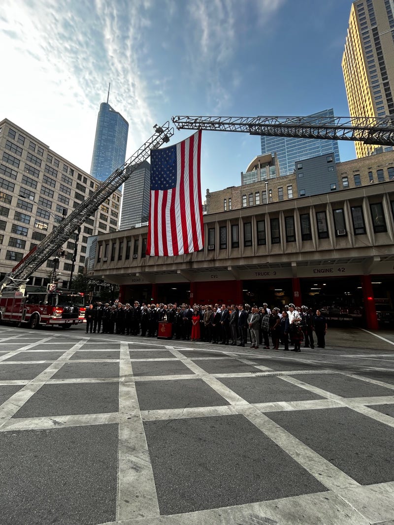 Outside Engine 42 in River North, city leaders and first responders stood shoulder to shoulder as two fire trucks stretched their ladders across Illinois Street, suspending a massive American flag. 
