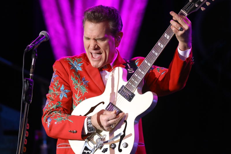 Musician and singer Chris Isaak performs in a red suit with a white guitar