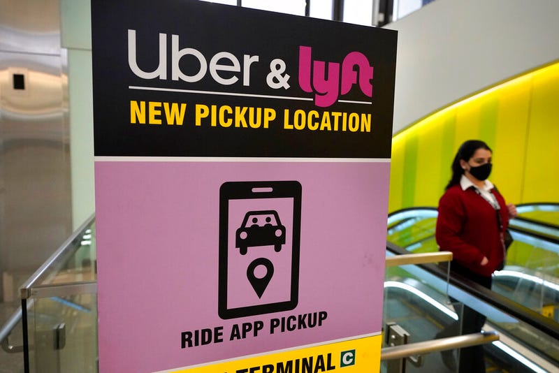 FILE - In this Feb. 9, 2021 file photo, a passer-by walks past a sign offering directions to an Uber and Lyft ride pickup location at Logan International Airport, in Boston. Uber and Lyft have teamed up to create a database of drivers ousted from their ride-hailing services for complaints about sexual assault and other crimes that have raised passenger-safety concerns for years. The clearinghouse unveiled Thursday, March 11, will initially list drivers expelled by the ride-hailing rivals in the U.S. But it will also be open to other companies that deploy workers to perform services such as delivering groceries or take-out orders from restaurants