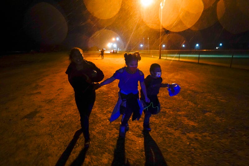 In this May 11, 2021, file photo, three young migrants hold hands as they run in the rain at an intake area after turning themselves in upon crossing the U.S.-Mexico border in Roma, Texas. The Biden administration says the number of unaccompanied migrant children housed at its largest emergency shelter has dropped by more than 40% since mid-June.