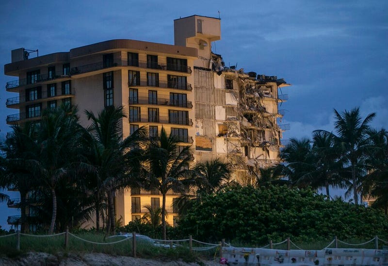 In this June 30, 2021, file photo, light shines on the Champlain Towers South as search and rescue teams continue looking for survivors of the partially collapsed residential building in Surfside, Fla. Dozens of people escaped with their lives, but little else. The disaster that killed at least 18 people, with more than 140 still missing, has also left many survivors homeless.