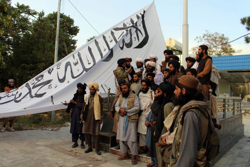 Taliban fighters poses for a photograph while raising their flag Taliban fighters raise their flag at the Ghazni provincial governor's house, in Ghazni, southeastern, Afghanistan, Sunday, Aug. 15, 2021.