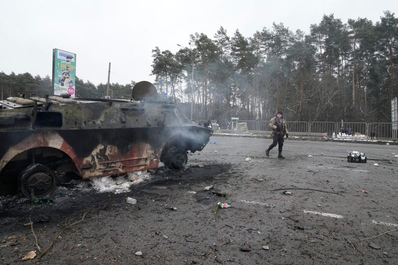 A volunteer of Ukraine's Territorial Defense Forces walks by a damaged armored vehicle at a checkpoint in Brovary, outside Kyiv, Ukraine, Tuesday, March 1, 2022