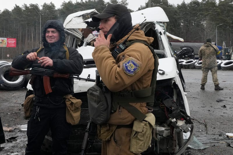 Armed men smoke by a damaged vehicle at a checkpoint in Brovary, outside Kyiv, Ukraine, Tuesday, March 1, 2022