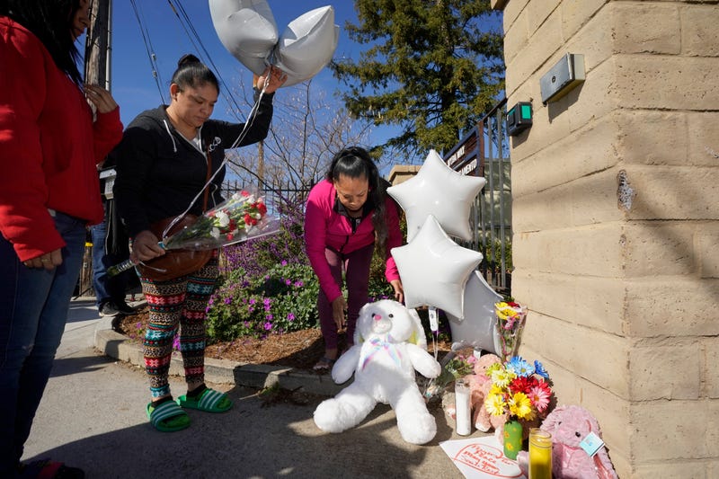 Ana DeJesus, right, places a teddy bear on a growing memorial at The Church in Sacramento, Calif., on Tuesday, March 1, 2022. At left, Vera Cruz waits to leave flowers and balloons. Authorities say a man shot and killed his three daughters, their chaperone and himself during a supervised visit with the girls at the church on Monday.