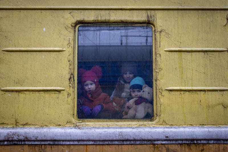 Children Vlada, left, Katrin and Danilo look out from a window of an unheated train carriage of an emergency evacuation train which is travelling from Kharkov to Lviv, as it stopped in the Kyiv railway station in Kyiv, Ukraine, Thursday, March 3, 2022