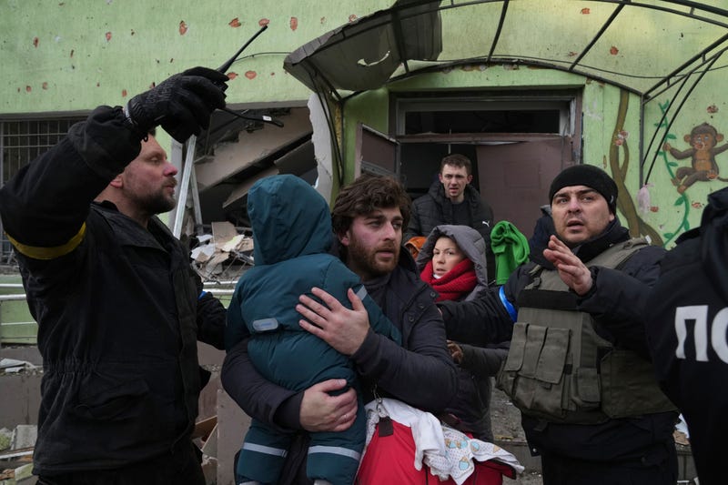 A man carries his child away from the damaged by shelling maternity hospital in Mariupol, Ukraine, Wednesday, March 9, 2022