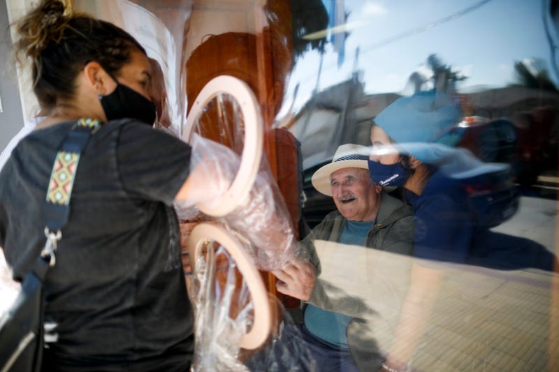 FILE - Debora Aberastegui holds the hands of her father Pedro Aberastegui through a plastic sleeve at the Reminiscencias residence for the elderly in Tandil, Argentina, Monday, April 5, 2021. Residents here do not have physical contact with their families or leave the residence due to the COVID-19 pandemic, but stay active with group activities within the facility.