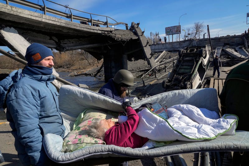 Volunteers pass an improvised path under a destroyed bridge as they evacuate an elderly resident in Irpin, some 25 km (16 miles) northwest of Kyiv, Friday, March 11, 2022