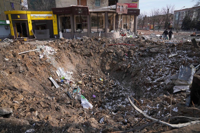 People walk past a crater from the explosion in Mira Avenue (Avenue of Peace) in Mariupol, Ukraine, Sunday, March 13, 2022