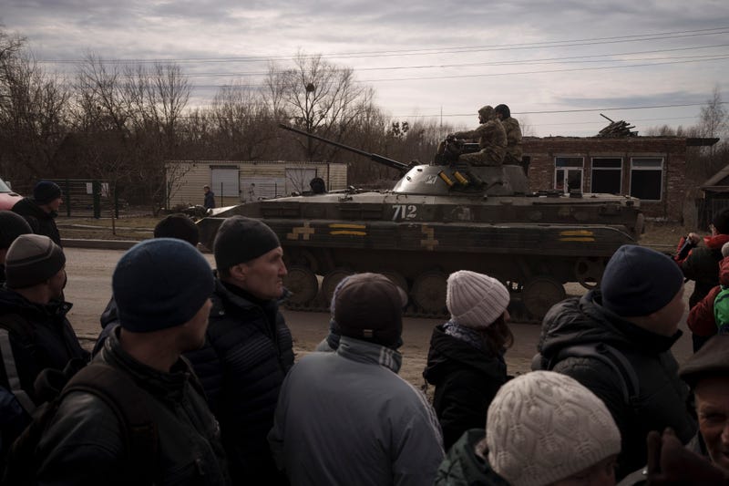 Residents lining up for aid watch as Ukrainian soldiers ride atop a tank in the town of Trostsyanets, Ukraine, Monday, March 28, 2022. Trostsyanets was recently retaken by Ukrainian forces after being held by Russians since the early days of the war.