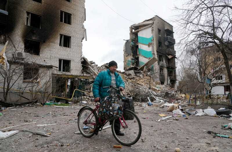 A man carries his belongings on a bike as he leaves his house, background, ruined in the Russian shelling in Borodyanka, Ukraine