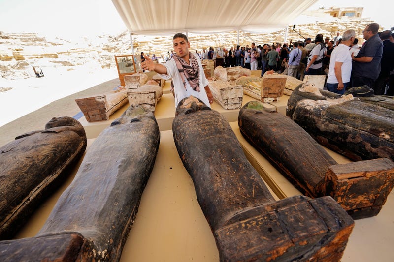 An antiquities employee tries to prevents reporters from getting close to painted coffins with well-preserved mummies inside