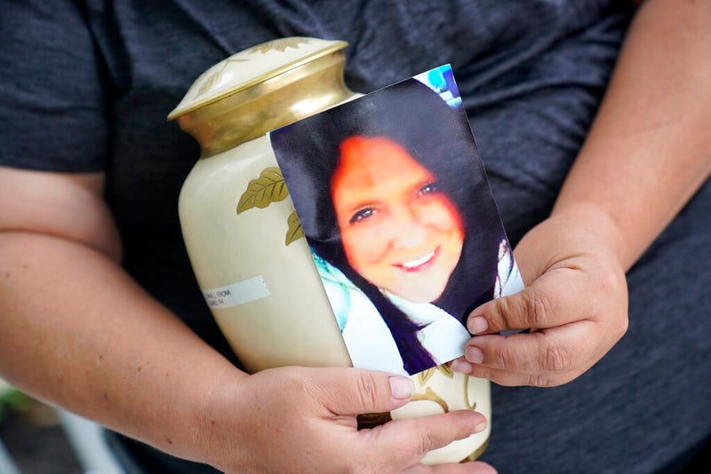 Kelly Titchenell sits on her porch in Mather, Pa., holding a photo of her mother Diania Kronk, and an urn containing her mother's ashes, Thursday, July 7, 2022. A Greene County, Pa., detective last week filed charges against 911 operator Leon “Lee” Price, 50, of Waynesburg, in the July 2020 death of Diania Kronk, 54, based on Price's reluctance to dispatch help without getting more assurance that Kronk would actually go to the hospital.