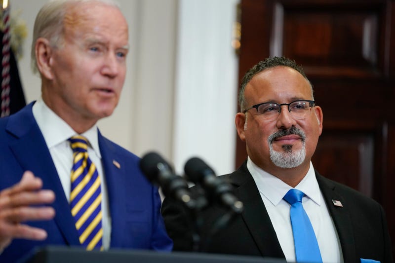 Education Secretary Miguel Cardona listens as President Joe Biden speaks about student loan debt forgiveness in the Roosevelt Room of the White House, Aug. 24, 2022, in Washington.