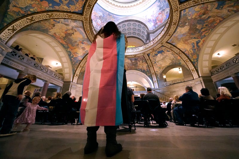Glenda Starke wears a transgender flag as a counter protest during a rally in favor of a ban on gender-affirming health care legislation, March 20, 2023, at the Missouri Statehouse in Jefferson City, Mo. A Missouri judge said Friday, Aug. 25, that a law banning gender-affirming treatments for minors can take effect. St. Louis Circuit Judge Steven Ohmer ruled that the law will kick in Monday, Aug. 28, as previously scheduled.