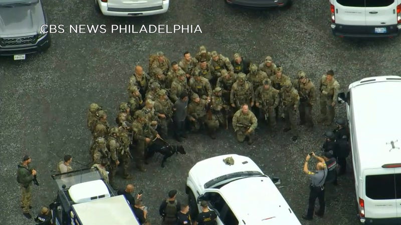 In this image from video provided by CBS News Philadelphia, law enforcement officers pose for a group photo with Danelo Cavalcante after his capture in Chester County.