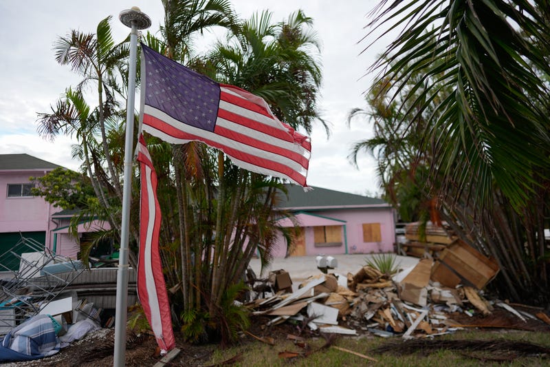 A tattered American flag flaps outside a home as furniture and household items damaged by Hurricane Helene flooding sit piled along the street awaiting pickup, ahead of the arrival of Hurricane Milton, in Holmes Beach on Anna Maria Island, Fla., Tuesday, Oct. 8, 2024.