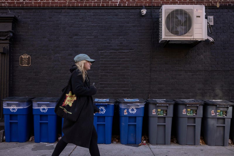 A person walks in front of trash bins, Friday, Nov. 15, 2024, in the Brooklyn borough of New York