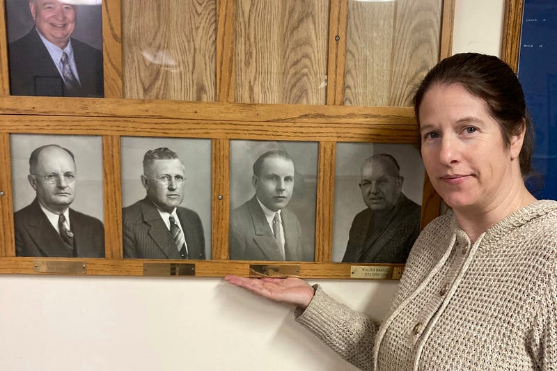 In this photo provided by Dan Donaldson, Dana Klabenes, the city clerk in Neligh, Neb., holds her hand under a photo of former Mayor Fred Benning, a World War I veteran who is being honored by having an Army base in Georgia renamed Fort Benning in his honor, at city hall on Tuesday, March 4, 2025.