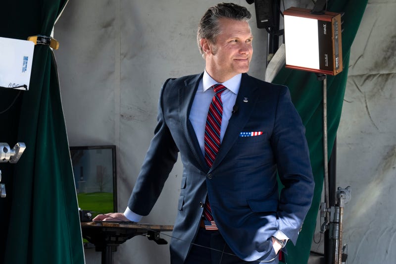 Wearing a U.S. flag themed pocket square and belt buckle, Defense Secretary Pete Hegseth waits for the start of a television interview outside the White House, Friday, March 21, 2025, in Washington.