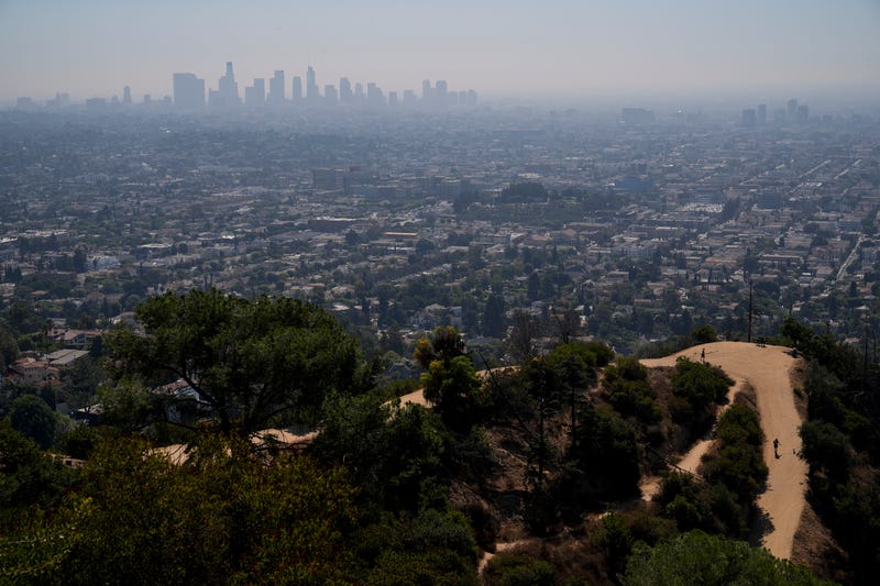 FILE - A person with a dog walks along a trail as a layer of smog blankets downtown Los Angeles, Tuesday, Oct. 1, 2024.