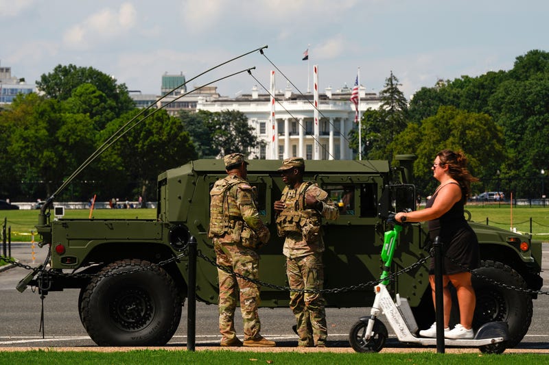 Members of the District of Columbia National Guard patrol in front of the White House as a woman rides past on a scooter, Saturday, Aug. 16, 2025, in Washington.