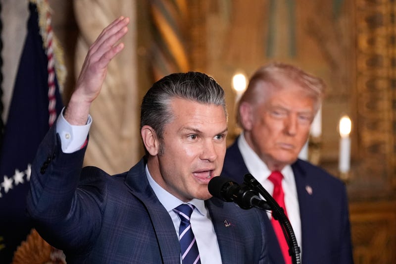 Defense Secretary Pete Hegseth speaks as President Donald Trump looks on, at Trump's Mar-a-Lago club, Monday, Dec. 22, 2025, in Palm Beach, Fla.